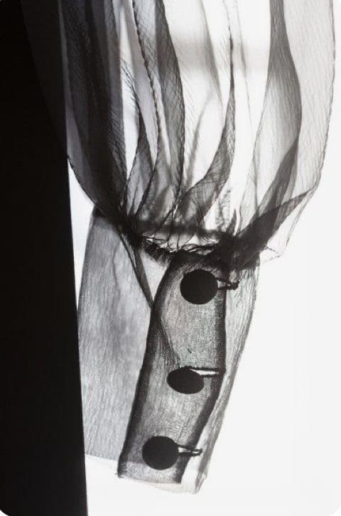 An X-ray-style photograph of a sheer organza sleeve cuff with three buttons
